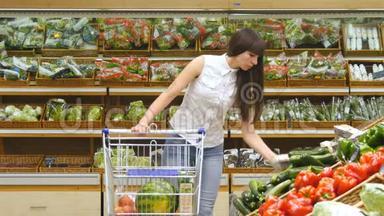 年轻女子推着手推车沿着超市的<strong>杂货</strong>店过道。 在<strong>杂货</strong>店选择新鲜蔬菜的女孩