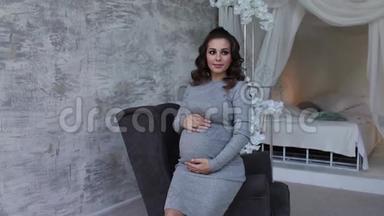 <strong>美丽</strong>的孕妇坐在扶手椅上，双手放在肚子上。 女人穿着优雅的衣服。 <strong>美丽美丽</strong>