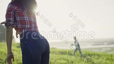 夏天，穿着蓝色牛仔裤的年轻女子在高高的小山上的草地上向太阳投掷<strong>飞盘</strong>，动作缓慢