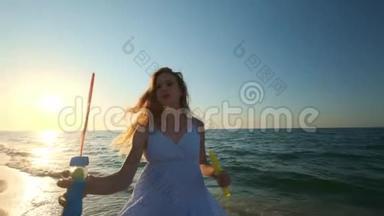 女孩在海滩上缓慢地吹泡泡。 傍晚，日落时，一个小女孩吹肥皂泡. 一路奔跑