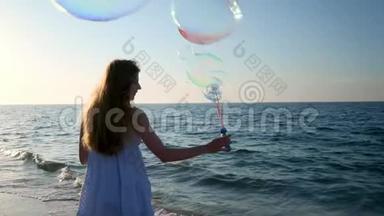 女孩在海滩上缓慢地吹泡泡。 傍晚，日落时，一个小女孩吹肥皂泡. 一路奔跑