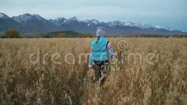 小女孩走在麦田里。 孩子奔跑的背景是美丽的山脉和白雪覆盖的山峰。 儿童