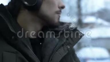 一位身穿夹克衫、戴着大耳机的长胡子青年坐在电车旁的公共交通工具里