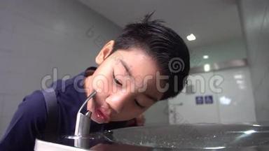 亚洲饥饿的男孩从水管里喝水。