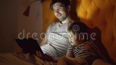 年轻的<strong>父亲和</strong>他的小<strong>儿子</strong>晚上躺<strong>在家里</strong>，用平板电脑看卡通电影