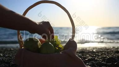 海滩上的水果篮。手在海浪的背景下从葡萄串中取出葡萄