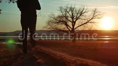 日落时分，一个人在路上奔跑，独自站在树上剪影。 运动的年轻人在大自然中奔跑