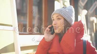 穿着红色冬装的漂亮女人站在满是雪的街道上，在一个晴朗的<strong>日</strong>子里用智能<strong>手机</strong>聊天