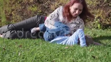 幸福的家庭在草坪上休息。 母亲用温柔和爱拥抱她的孩子，儿子笑了。 快乐的童年