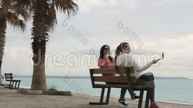 两个年轻的女人坐在海边，用智能<strong>手机手机</strong>相机<strong>拍摄</strong>自己的肖像。 特写镜头。 高清高清