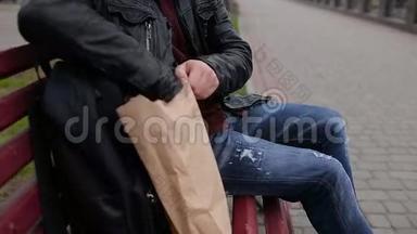年轻人坐在长椅上吃热狗