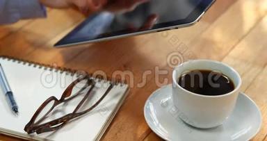 女商人在桌子上使用数字平板电脑，桌子上放着一杯咖啡、眼镜和笔记本