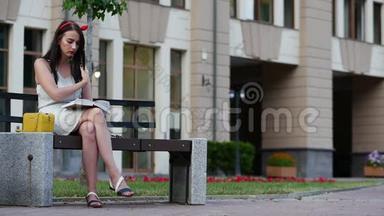 可爱的女孩，头上有一个红色的边缘，坐在公园的长凳上读一本书。