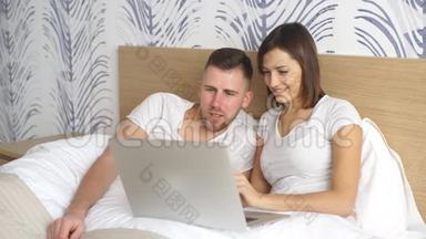 年轻夫妇带着笔记本电脑<strong>在床上</strong>看电影