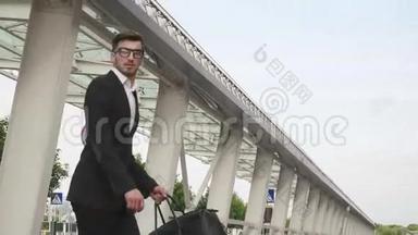 年轻的商人戴着眼镜，留着胡子，带着一个大大的手提箱慢动作地跑到他的飞机上。 城市