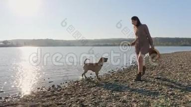 可爱的年轻女人和她可爱的狗在湖边的大自然中玩耍。