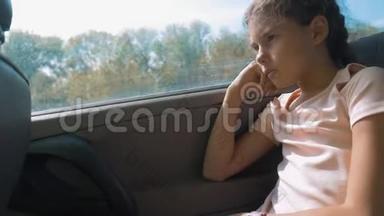 伤心的女孩无聊地坐在车后座上运动旅行。 小女孩在车里无聊。 概念生活方式