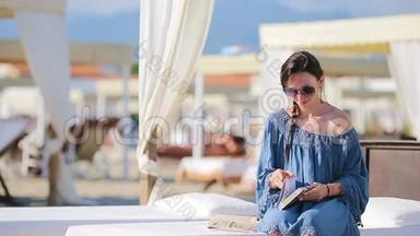 年轻女子在热带海滩度假期间<strong>看书</strong>。 时尚女郎坐在欧洲海滩的白色日光浴<strong>床上看书</strong>