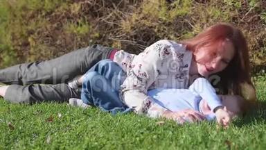 幸福的家庭在草坪上休息。 母亲用<strong>温柔</strong>和爱拥抱她的<strong>孩子</strong>，儿子笑了。 快乐的童年