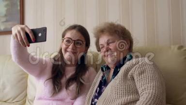 奶奶和年轻女孩在家里坐在沙发或沙发上用手机或智能手机拍照。 快乐的女士们
