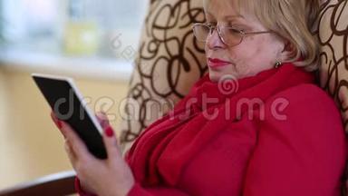 老妇人坐在沙发上用电子书。 带电子书的女人