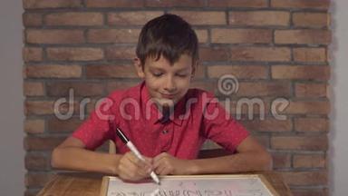 坐在办公桌前的孩子拿着一张挂图，背景红砖墙上有刻字的签名。