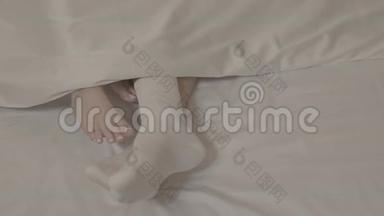 男人的双腿穿着白色的袜子，两个女人光着脚躺在床上，躺在白色的床单上，紧紧地躺在毯子下面