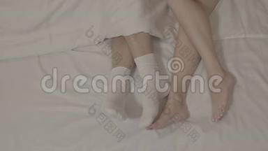 男人的双腿穿着白色的袜子，两个女人光着脚躺在床上，躺在白色床单上的毯子上，紧紧地躺在床上