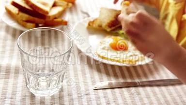 一个孩子正在吃早餐（炒鸡蛋、烤面包和沙拉），而一个<strong>家长</strong>则把橙汁倒进他的杯子里