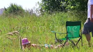 一个穿泳衣的女孩正在草坪上晒日光浴。 在她旁边的野<strong>餐椅</strong>上，一个男人坐在智能手机里玩。