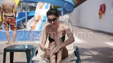 在泳池附近的日光浴床上涂防晒霜的漂亮女人
