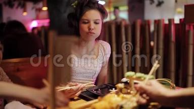 泛亚餐厅的家庭晚餐。 女孩用筷子吃面包。 在餐厅里摆着寿司和卷