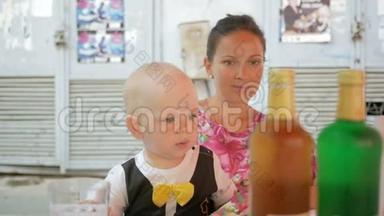 <strong>妈妈和宝宝</strong>穿着一件漂亮的裙子<strong>和</strong>蝴蝶在街上的咖啡馆里吃饭。 有青黄柠檬水的银行