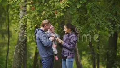 快乐的家庭：爸爸、妈妈和小女孩在秋天公园：爸爸、妈妈和宝宝在罗文身边摆姿势