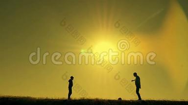 日落时分，父亲和儿子在公园里踢足球，在灿烂的阳光下剪影