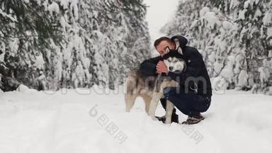 一个男人在森林里拥抱他的西伯利亚哈士奇。 在<strong>雪</strong>地里的背景树上。 眼中的骄<strong>傲</strong>和幸福.. 步行