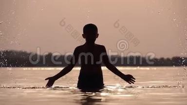 日落时快乐男孩的剪影，用他的手创造了溅水。 慢动作