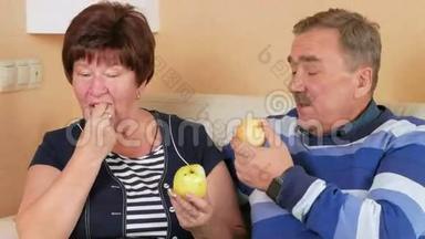老两口在家里躺在<strong>沙发</strong>上吃苹果。 桌子上有一盘不同的<strong>水果</strong>。 丈夫和