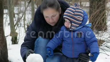 可爱的妈妈和宝宝在冬天的森林里雕刻小雪人。 圣诞假期的家庭乐趣