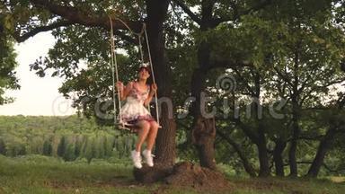 孩子们在公园的秋千上晒太阳。 年轻女孩在橡木树枝上的绳子上摆动。 少女喜欢飞行