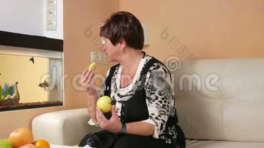 年老的女人在水族馆里吃苹果和看鱼。 <strong>桌子上</strong>有一盘不同的<strong>水果</strong>。 坐在里面