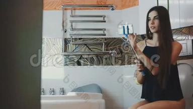 漂亮的女孩坐在浴室的厕所里，拿着蓝色的智能手机。