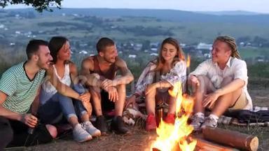 一群朋友坐在篝火旁，喝着<strong>热饮料</strong>和交谈