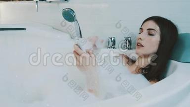 快乐的女孩在浴室里洗满泡沫的澡。 通过控制器切换音乐