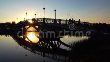 夏季日落时拱形公园桥和步行者的剪影。 4K视频