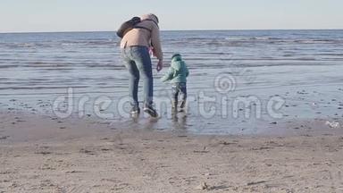 妈妈带着一个小孩沿着春天的海滩散步