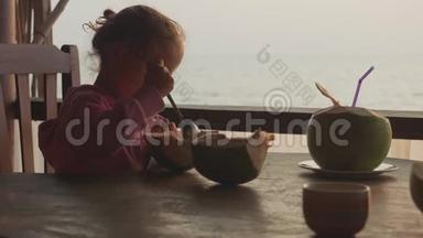 小可爱的女孩在咖啡馆用勺子吃椰子，海景慢镜头