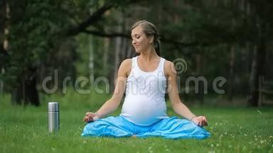 怀孕瑜伽在莲花的位置与热水瓶喝茶。 在公园的草地上，户外，健康的女人，女人。