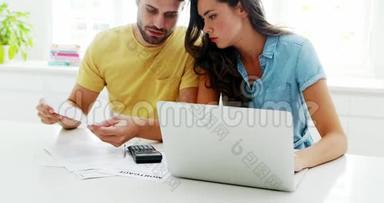 担心的夫妇在厨房里用笔记本电脑计算账单