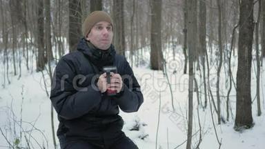 一个年轻人在冬天的森林里用热水瓶喝热饮料。那人在雪地里环顾四周，在树上